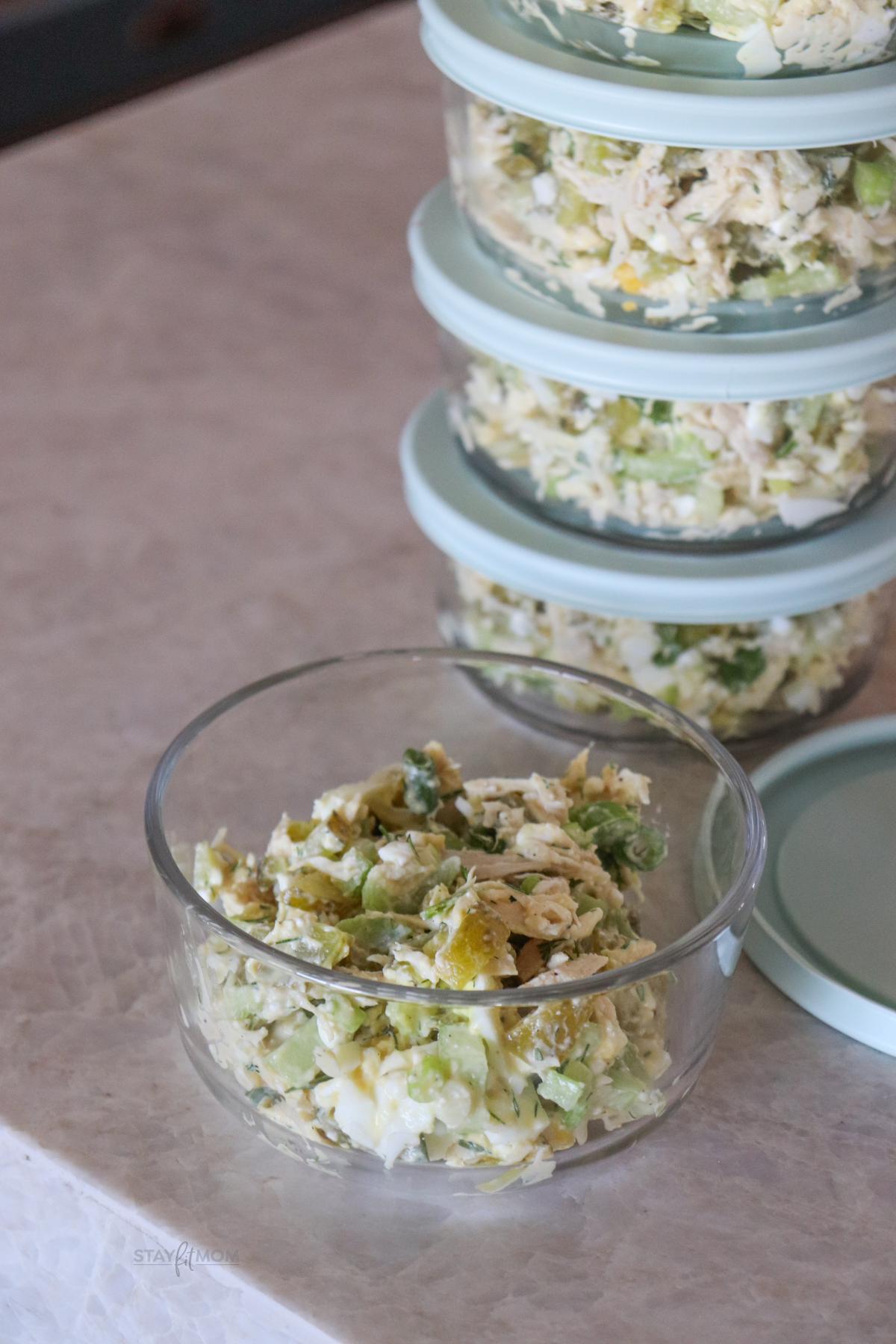 Dill chicken salad with completed recipe in a meal prep bowl without lid in front of 4 meal prep bowls stacked up behind it.