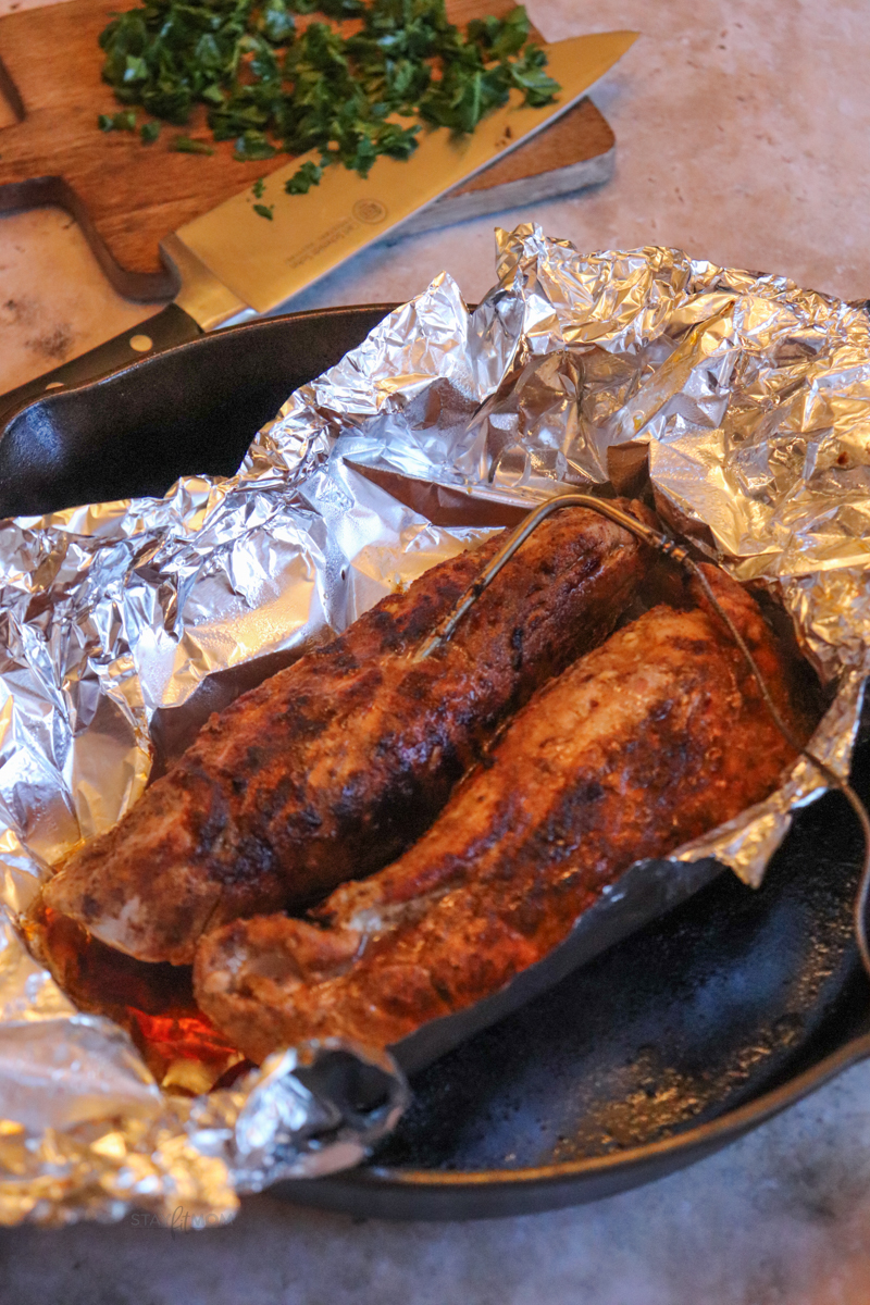 Pork tenderloin in tinfoil in a cast iron skillet with a meat thermometer after "resting" period.