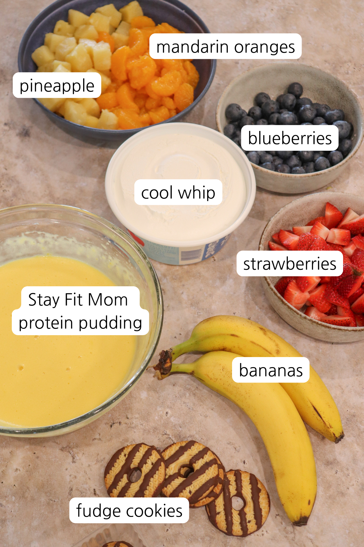 Cookie fruit salad with labeled ingredients showing: SFM protein pudding, bananas, strawberries, cool whip, blueberries, pineapple, and mandarin oranges.