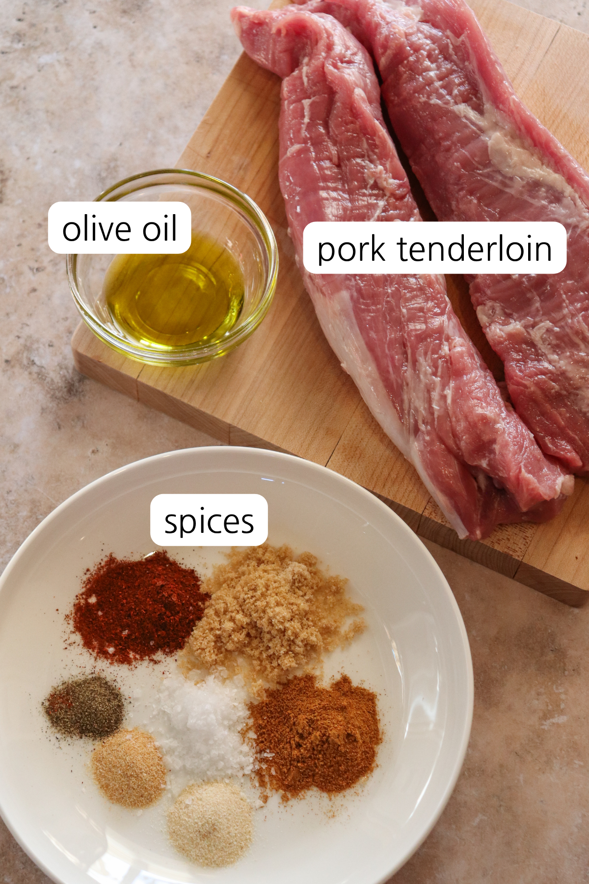 Pork tenderloin with ingredients in small bowls and labeled: olive oil, pork tenderloin, and spices.