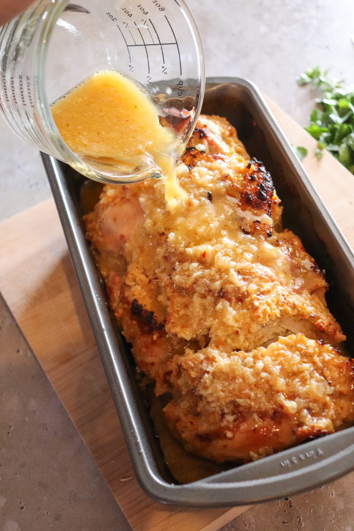 Crunchy onion loaf pan chicken showing cooked chicken in pan being topped with reserved oil.