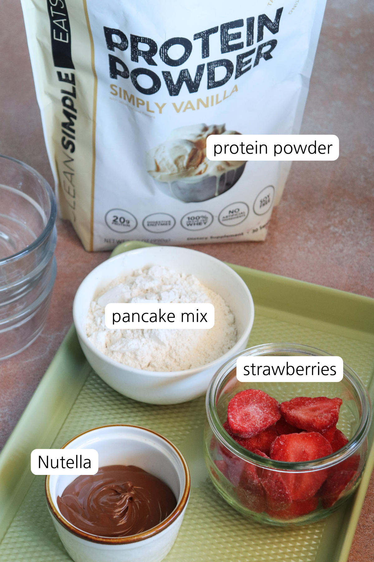 Real Strawberry Nutella Protein Pancake Bowls showing labeled ingredients: pancake mix strawberries, nutella, and protein powder.