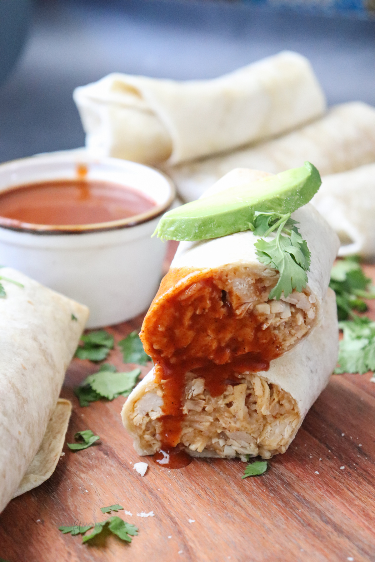 Cheesy Chicken & rice Burritos showing completed burrito cut in half, dipped in taco sauce and topped with a slice of avocado.