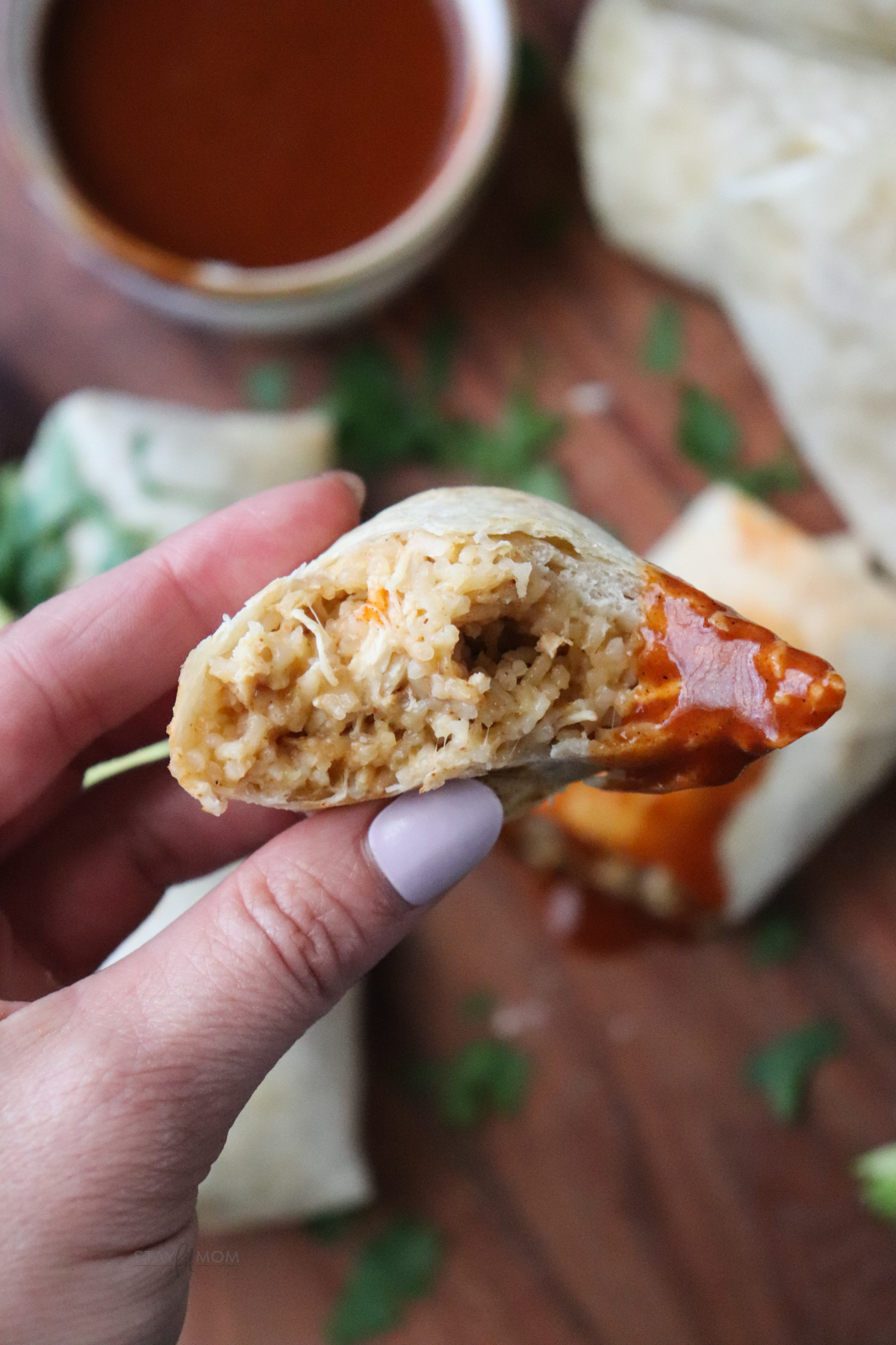 Cheesy chicken & rice burritos showing a bite of burrito dipped in taco sauce showing the cheesy chicken and rice mixture.