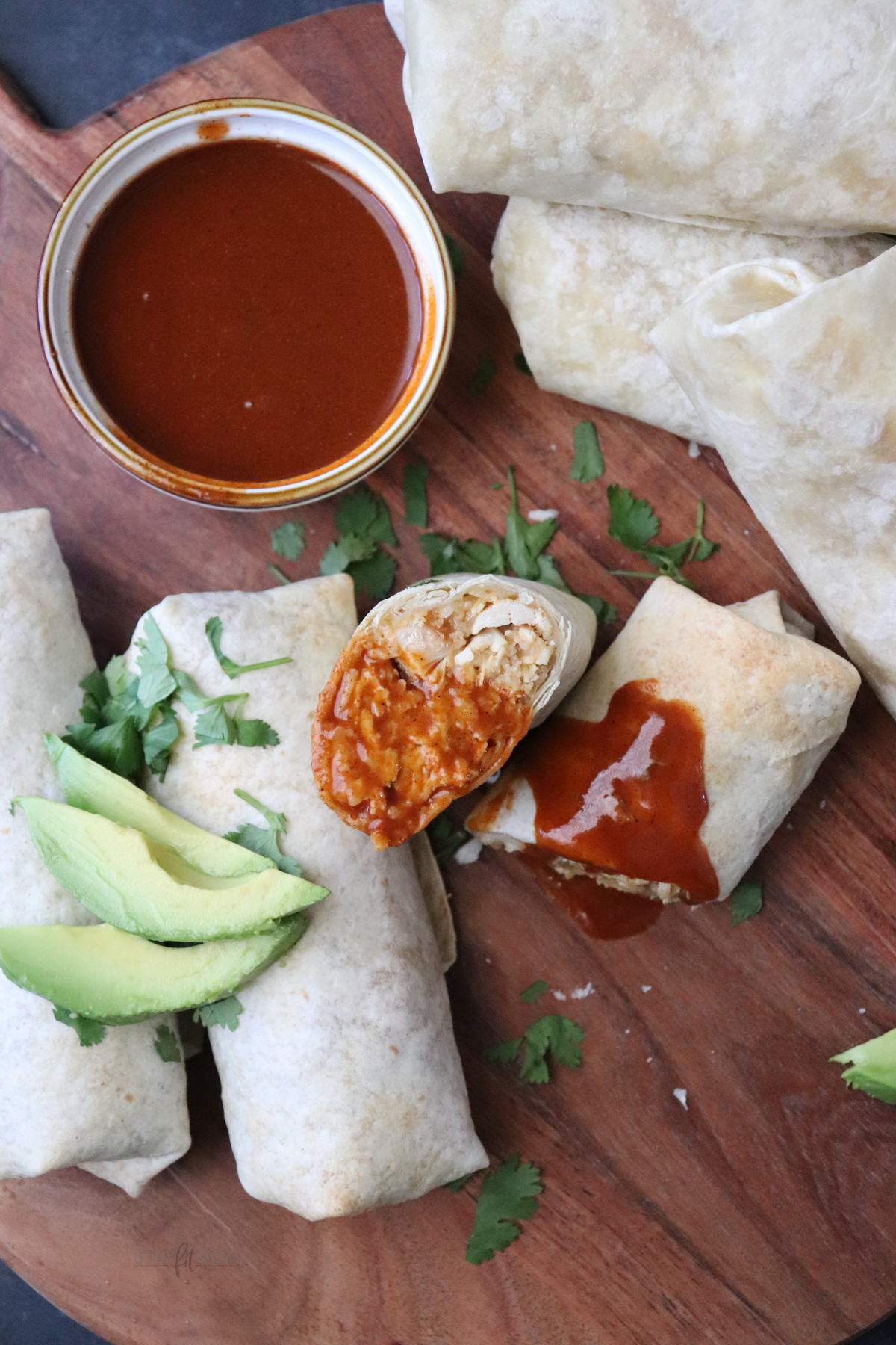 Cheesy Chicken & rice Burritos showing completed burrito cut in half, dipped in taco sauce and more burritos on the side topped with a slices of avocado.