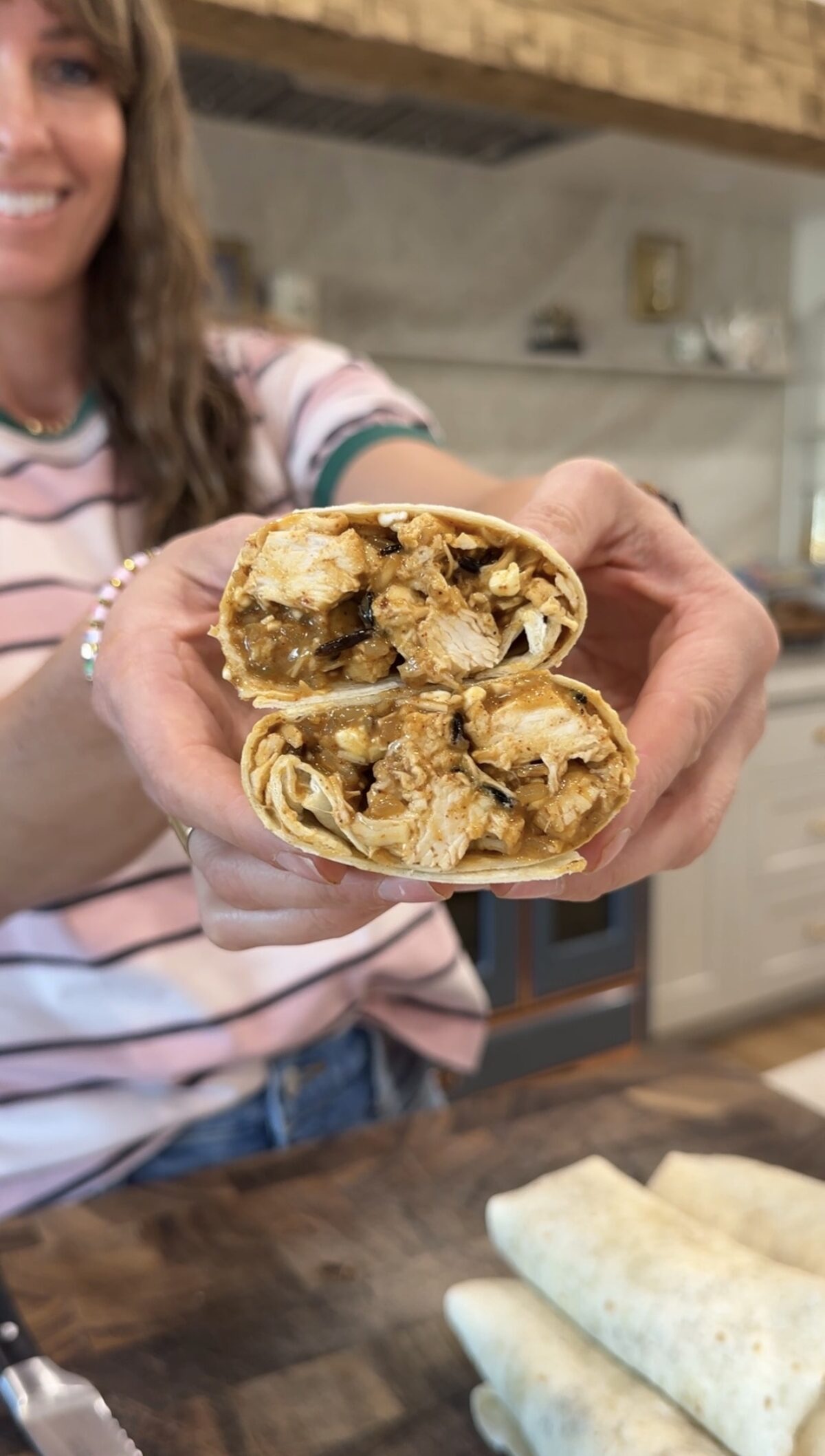 Krista holding a cheesy chicken & rice burrito cut in half and stacked on top of each other to show the inside of the burrito.
