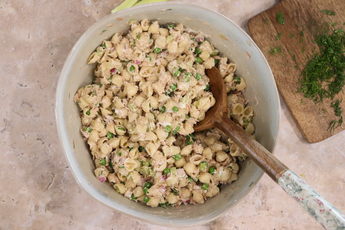 Tuna pasta salad showing a bowl of completed recipe with visible shell pasta, peas, celery, tuna and purple onion in a creamy sauce.