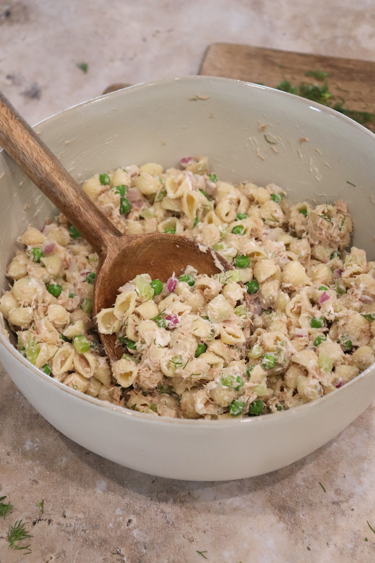 Tuna pasta salad showing a bowl of completed recipe with visible shell pasta, peas, celery, tuna and purple onion in a creamy sauce.