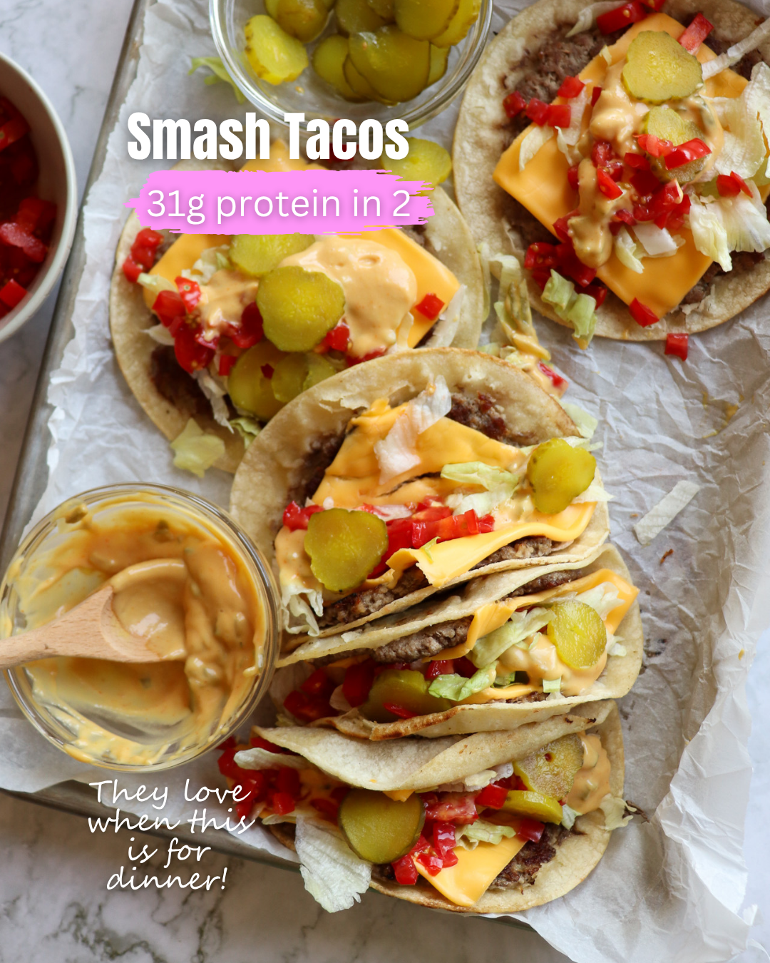 Smash Tacos showing a parchment lined pan with several smash tacos showing tortillas with ground beef, cheese, lettuce, tomatoes, pickles, and sauce.