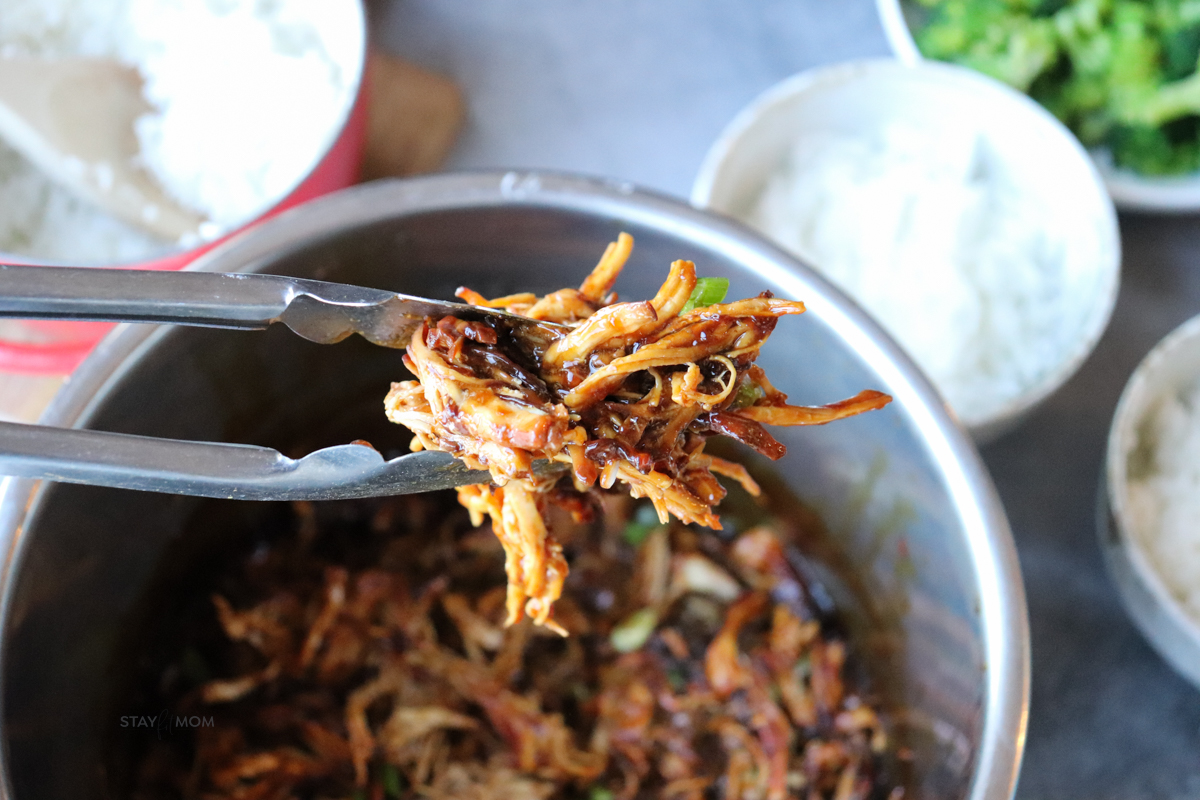 Silver tongs showing a bit of the perfectly shredded teriyaki chicken.