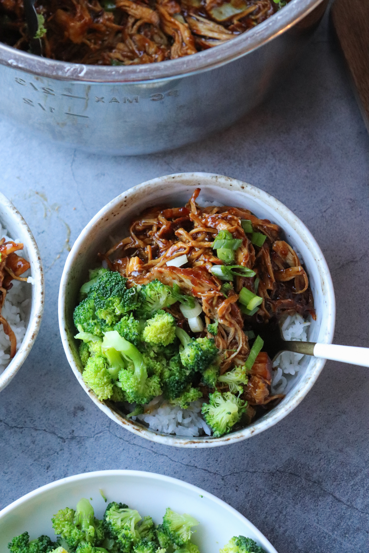 Teriyaki chicken showing completed recipe shredded on top of a bed or rice with broccoli.