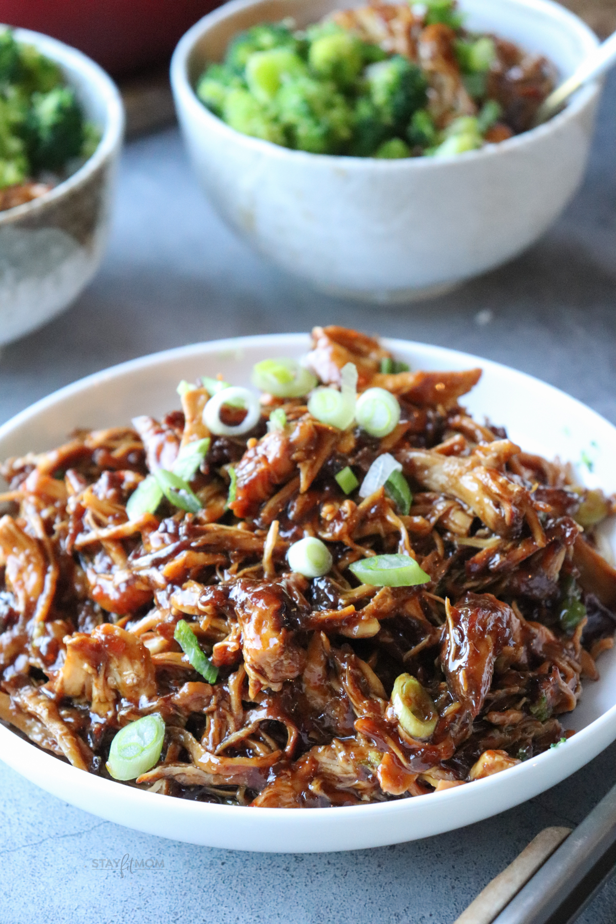 A white plate with a pile of delicious teriyaki chicken with scallions on top.
