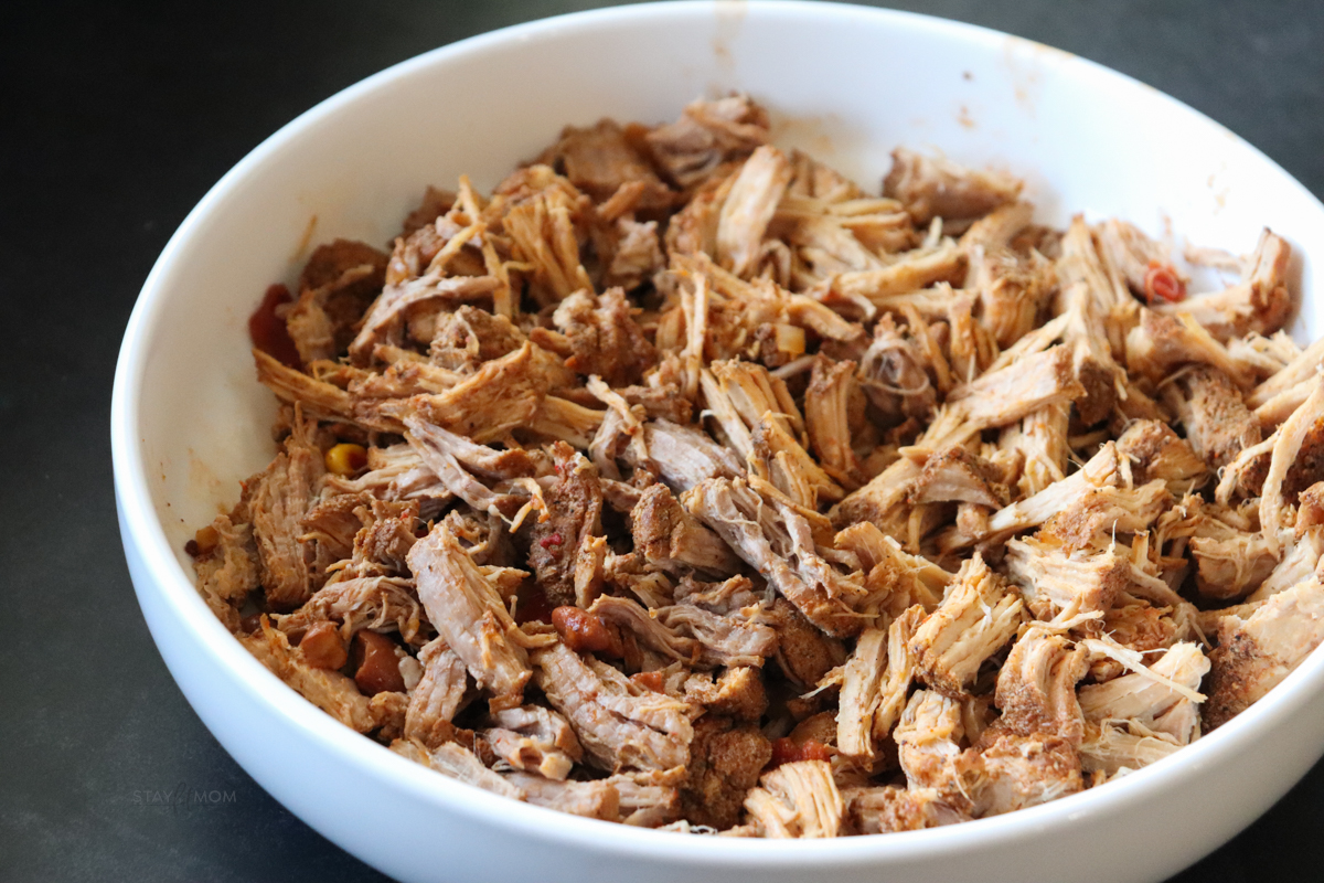 A white bowl filled with cooked, shredded pork loin.