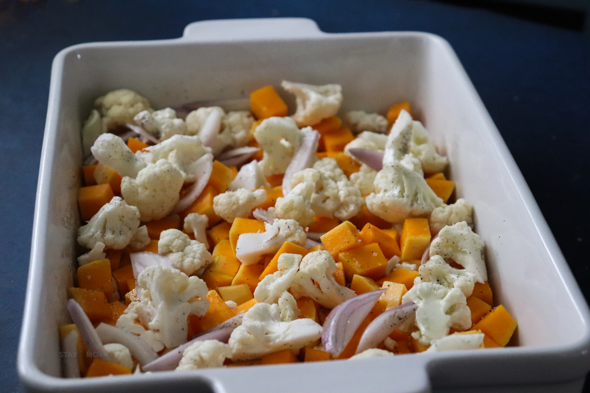 Sausage Butternut Casserole showing white baking dish loaded with diced butternut squash, cauliflower florets, and diced onions.