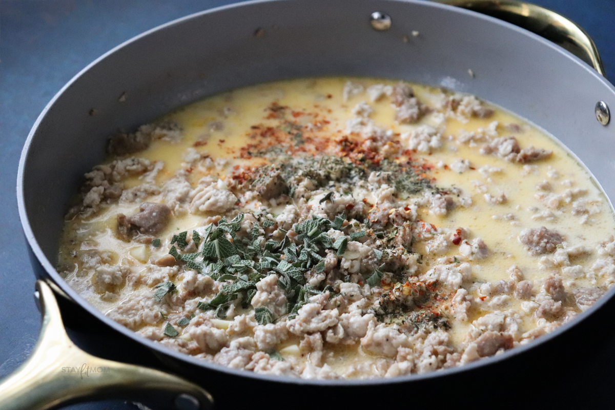 A skillet filled with sausage, spices, and sauce to be poured over the squash.