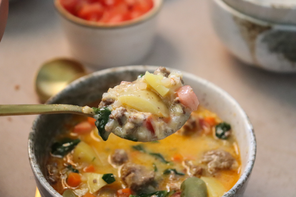 Cheeseburger soup with a spoonful in the foreground with the perfect bite showing potatoes, ground beef, spinach, and some toppings.