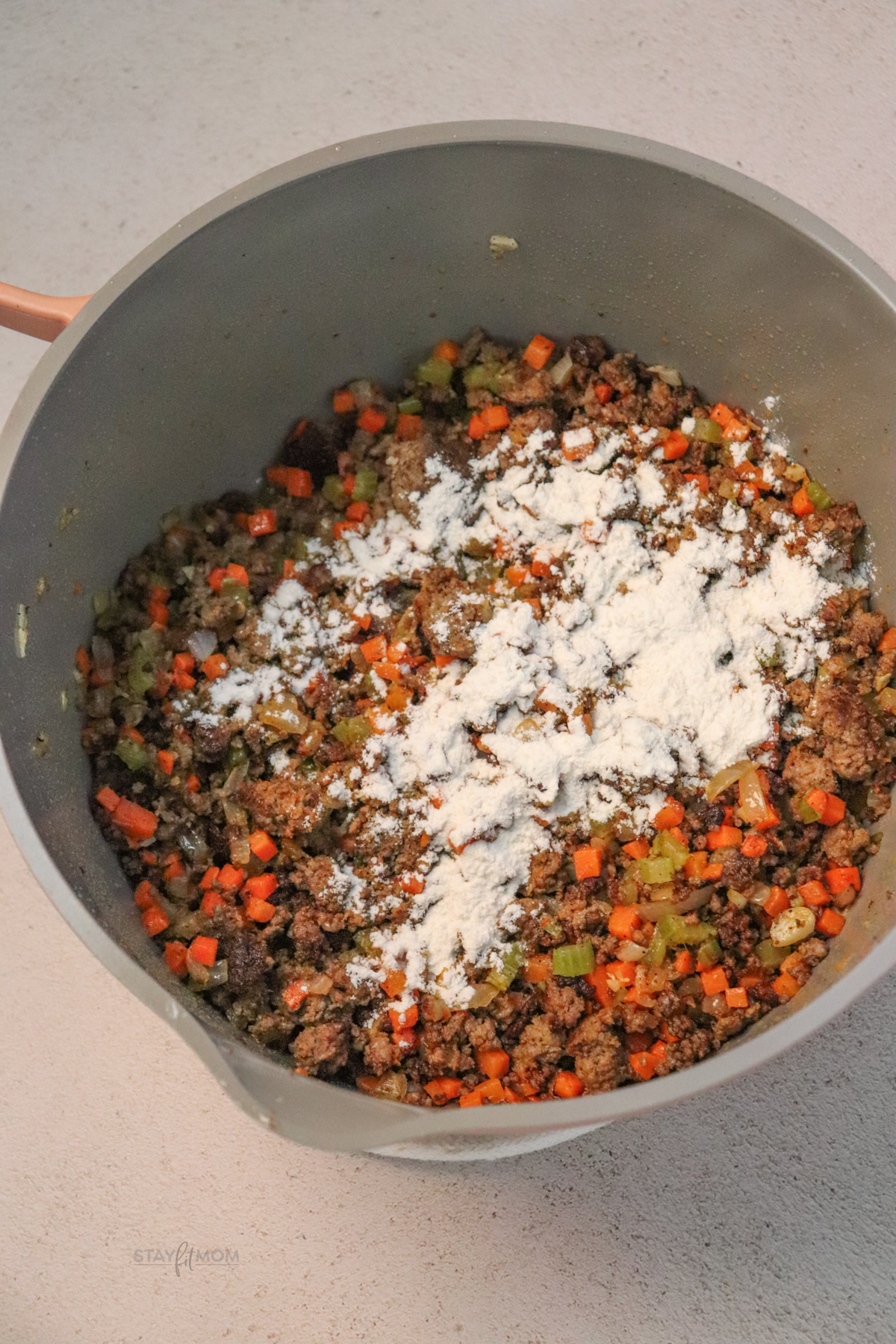 A pot filled with ground beef, diced veggies, and topped with flour ready to thicken.