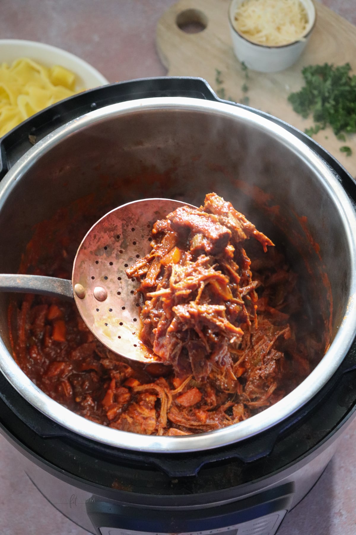 Beef Ragu showing Instant Pot with a spoon hovering over it showing a scoop of shredded beef and sauce.