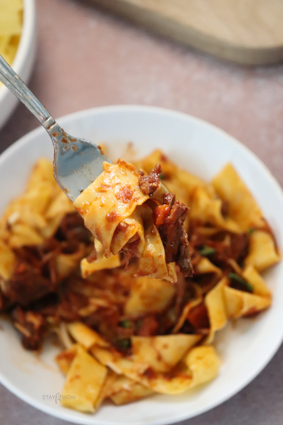 Beef Ragu being served over pasta with a forkful to show texture.