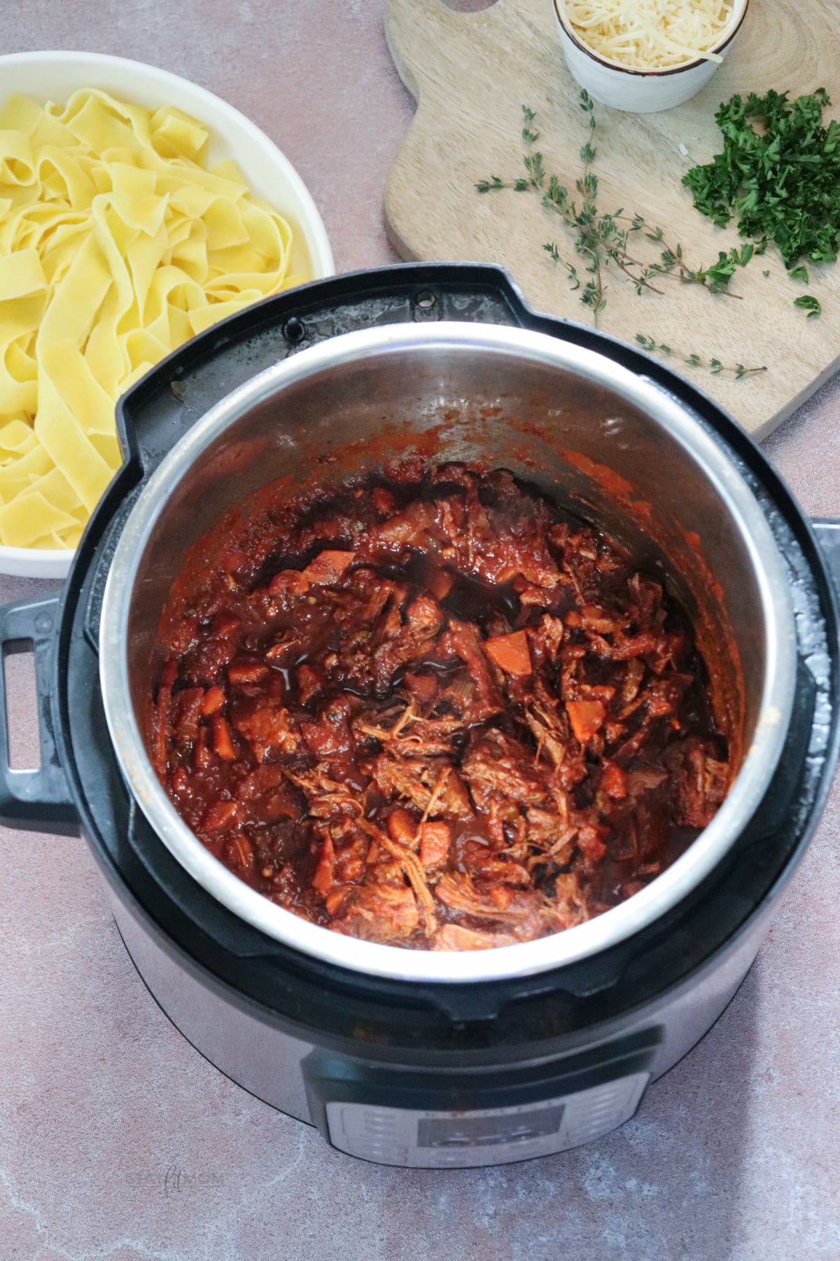 Beef Ragu showing Instant Pot with finished shredded beef in sauce and a white bowl with noodles behind it.
