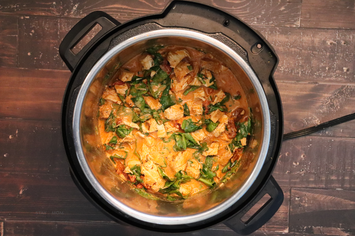 An overhead view of Marry Me Chicken showing an Instant Pot filled with finished recipe with chopped chicken in a red, creamy sauce topped with basil leaves.