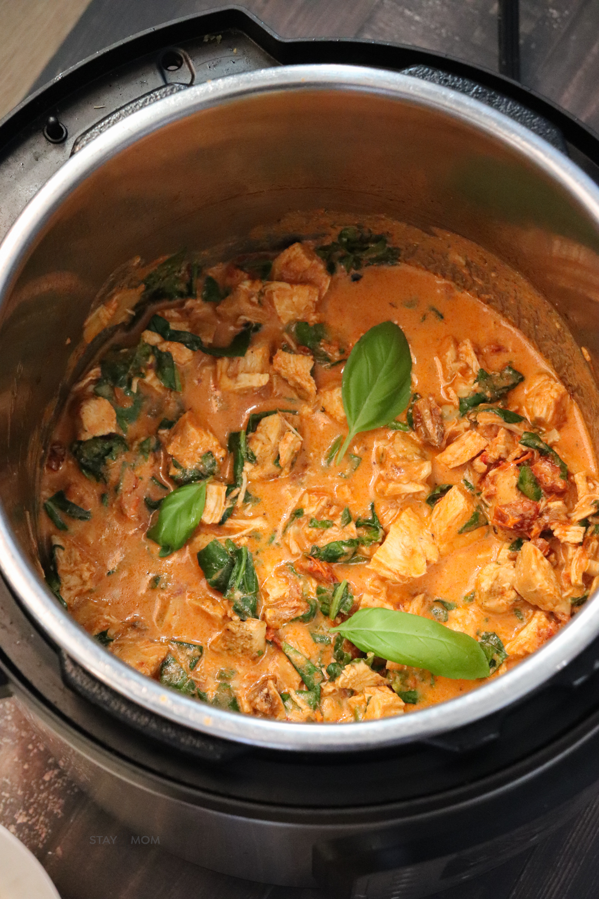 Marry Me Chicken showing an Instant Pot filled with finished recipe with chopped chicken in a red, creamy sauce topped with basil leaves.