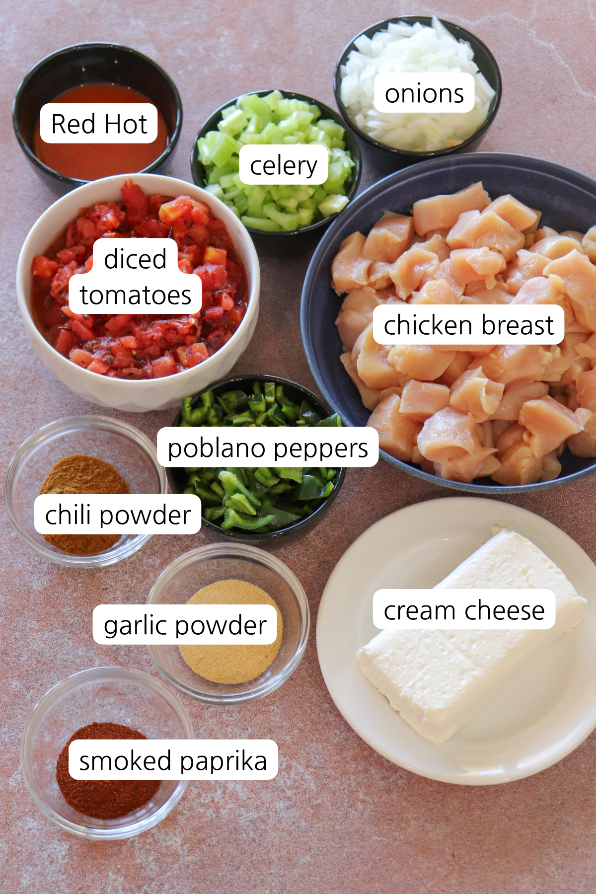 Small bowls labeled with ingredients: Red Hot, celery, onions, diced tomatoes, diced chicken breast, poblano peppers, chili powder, garlic powder, smoke paprika, and cream cheese.